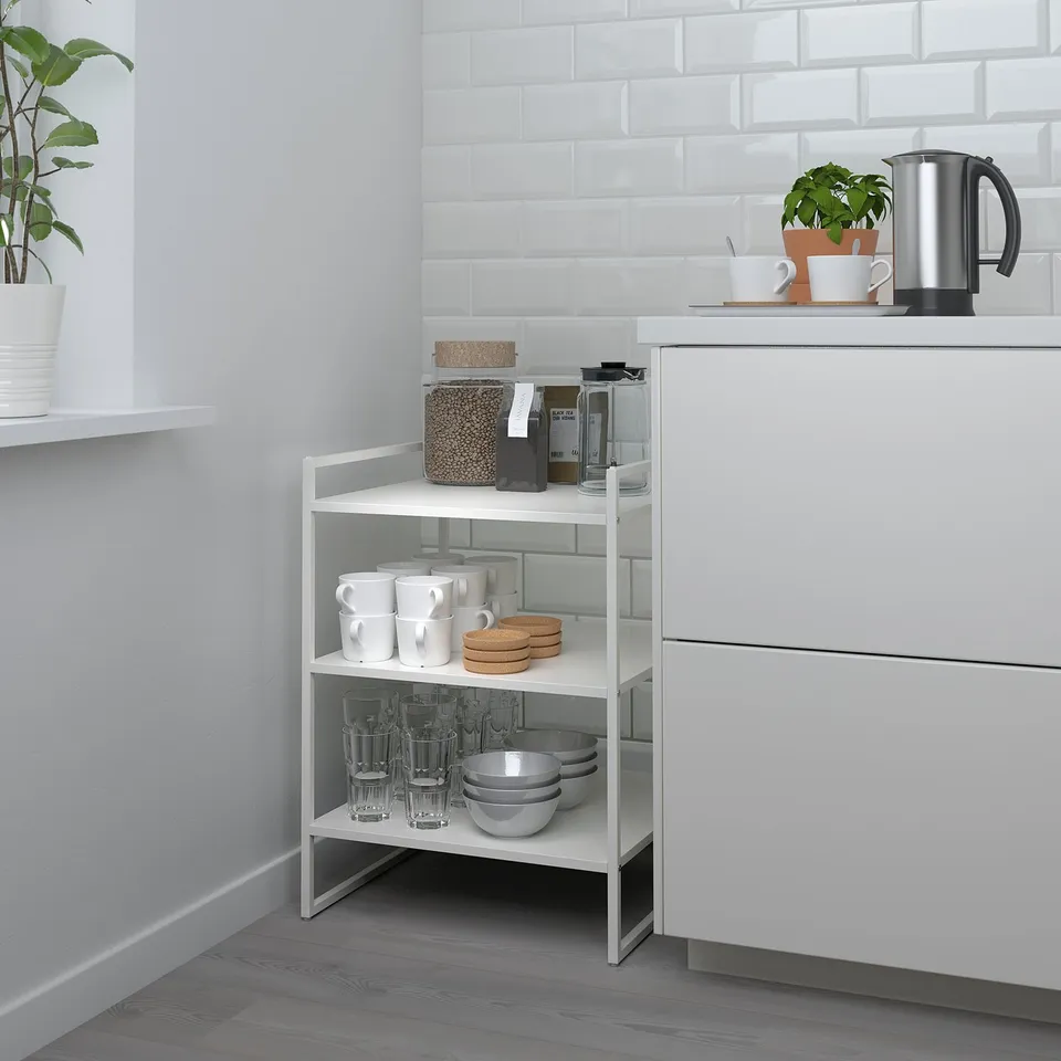 Modern white JONAXEL 3-tier shelving fits neatly in kitchen corner, holding cups, bowls, and glasses beneath a tiled backsplash.