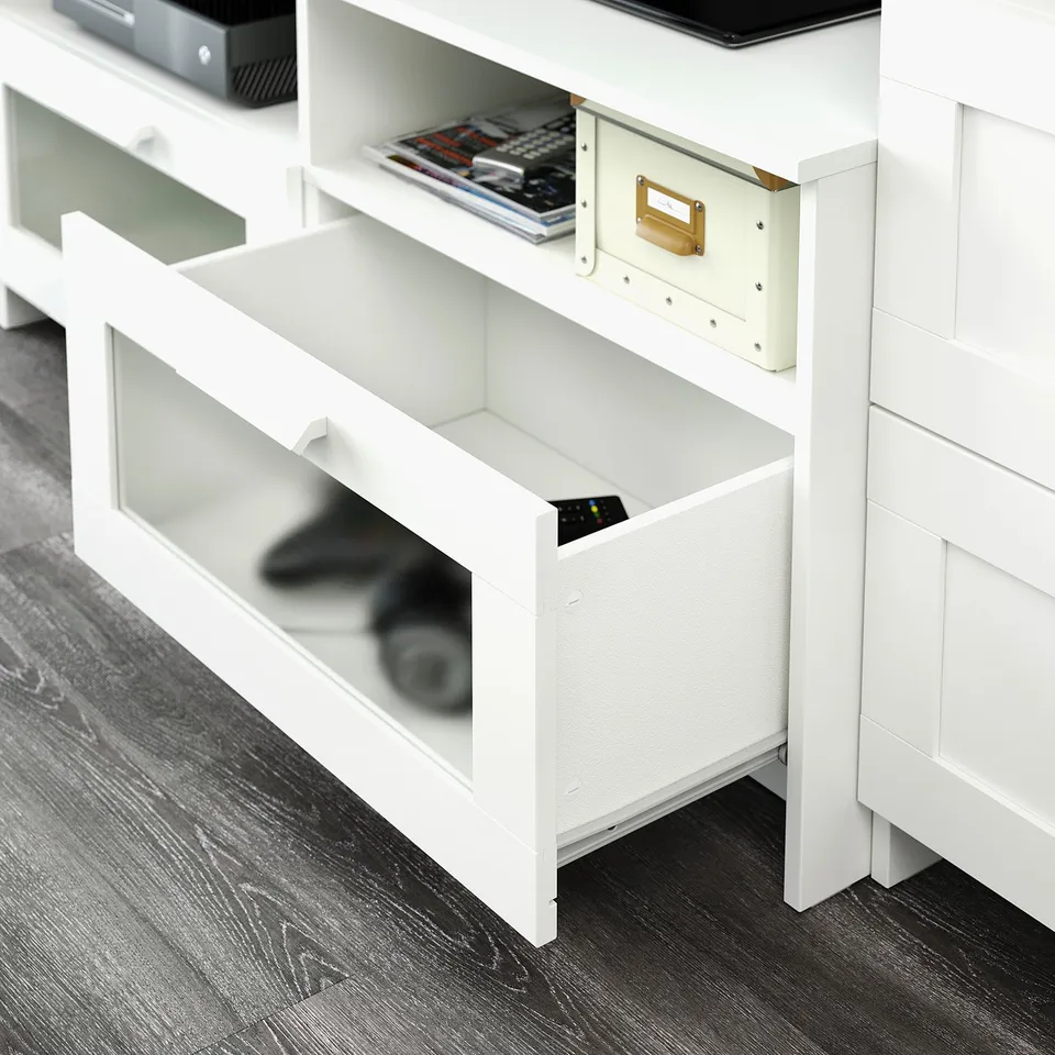 White tv stand with adjustable shelves, cable outlet, holding tv and media, showing storage and remote holder.