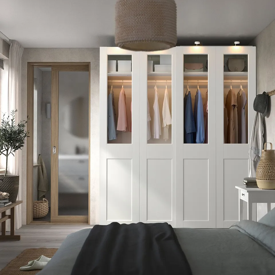 Modern bedroom with large white PAX wardrobe displaying colourful clothes and grey bed.
