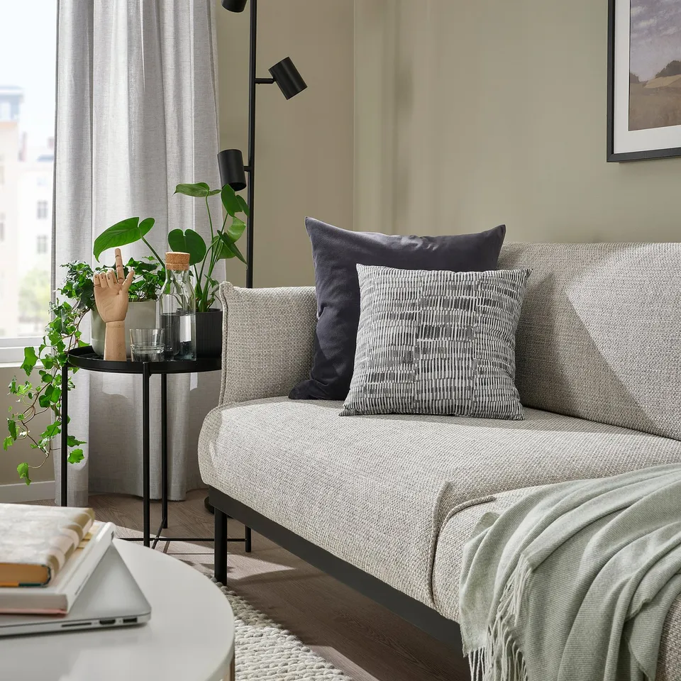 Modern living room with grey cushion, black side table, laptop, books, rug, and floor lamp.