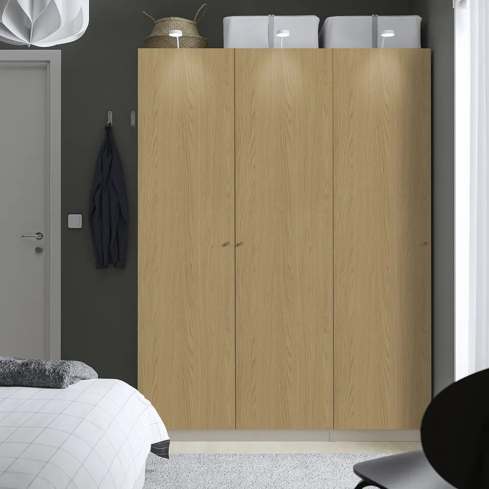Minimalist bedroom with large wooden PAX wardrobe, metallic handles, and hat on top.