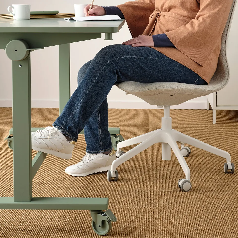 Person sitting at green foldable table with footrest, using white chair with casters.