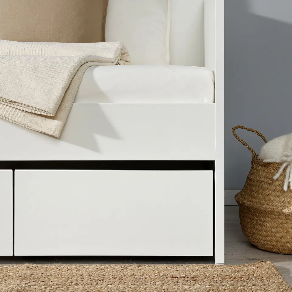 White daybed with storage, perfect for small spaces. Tidy bed with pillows and blanket, plus basket of throws.