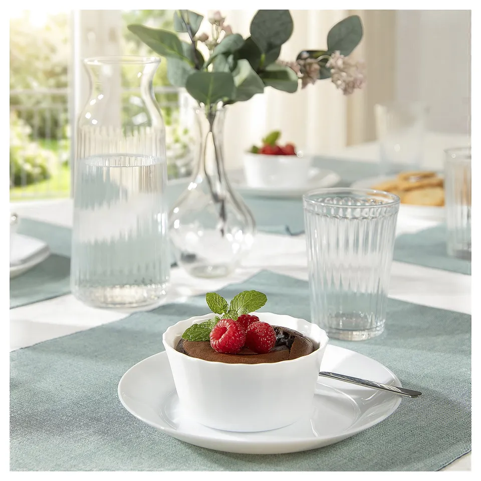 A dining table set with glassware, a white ceramic dish containing chocolate mousse and raspberries, placed on a blue placemat.