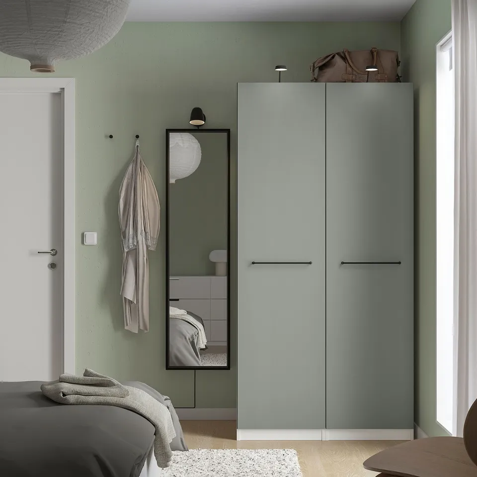 Green bedroom with grey wardrobe, mirror, bed, rug, YTBERG lamp, robe, bag, thermostat.