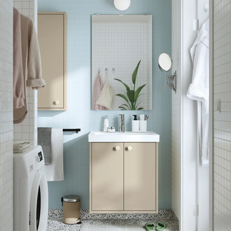 Modern bathroom with HAVBÄCK beige cabinet, two doors, washing machine, sink, mirror, plant, towels. Clean, minimalistic design.