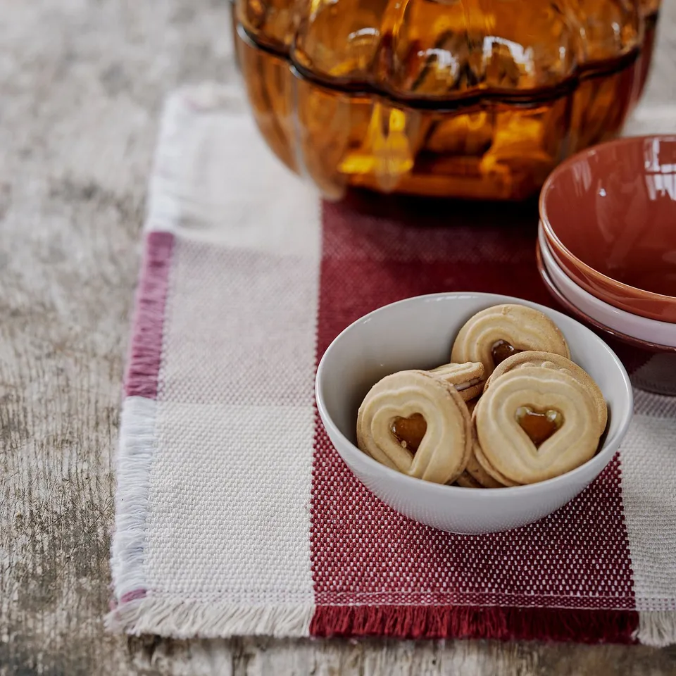 Small bowl of heart-shaped cookies on a white cloth place mat, set for a cosy autumn meal.
