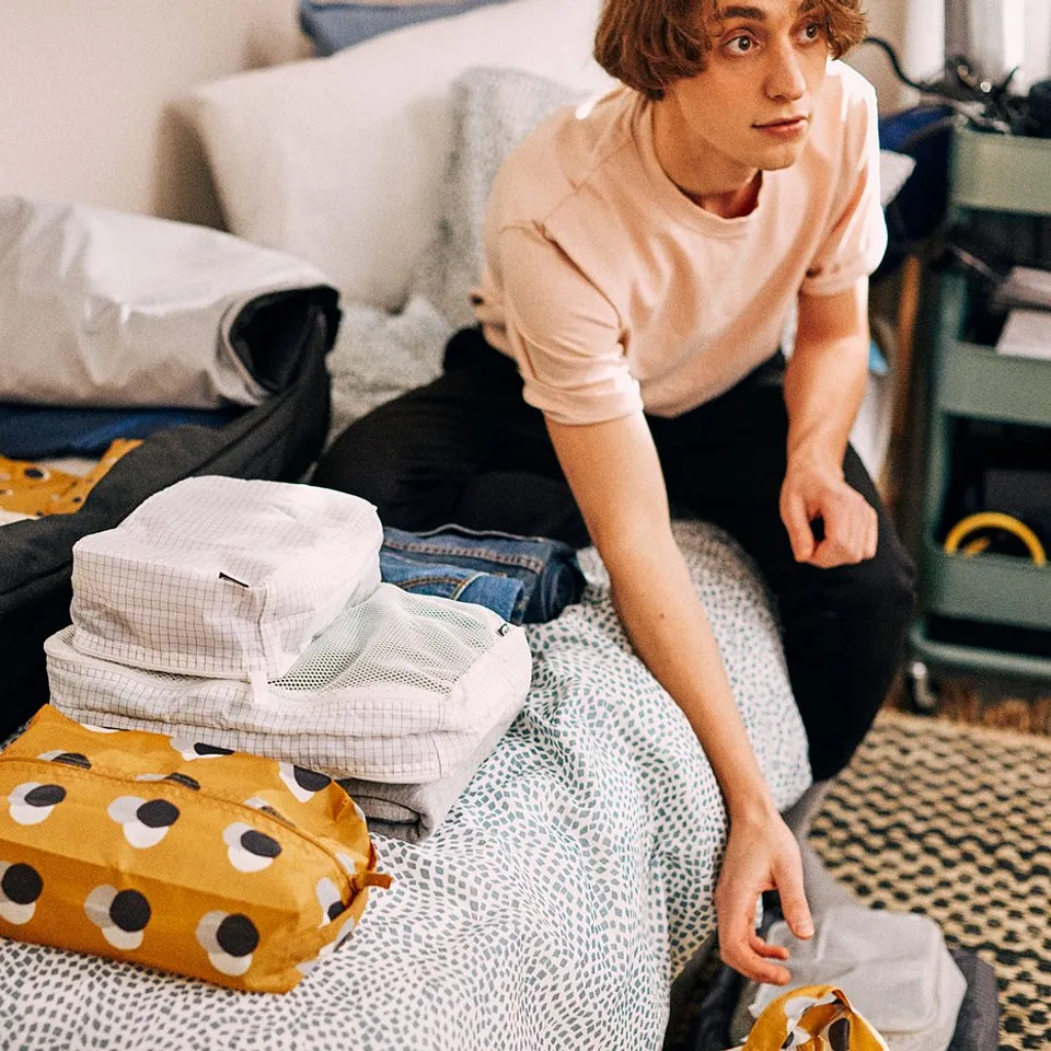 Young person packing clothes in colourful, patterned RENSARE packing cubes on a bed, ensuring organised travel.