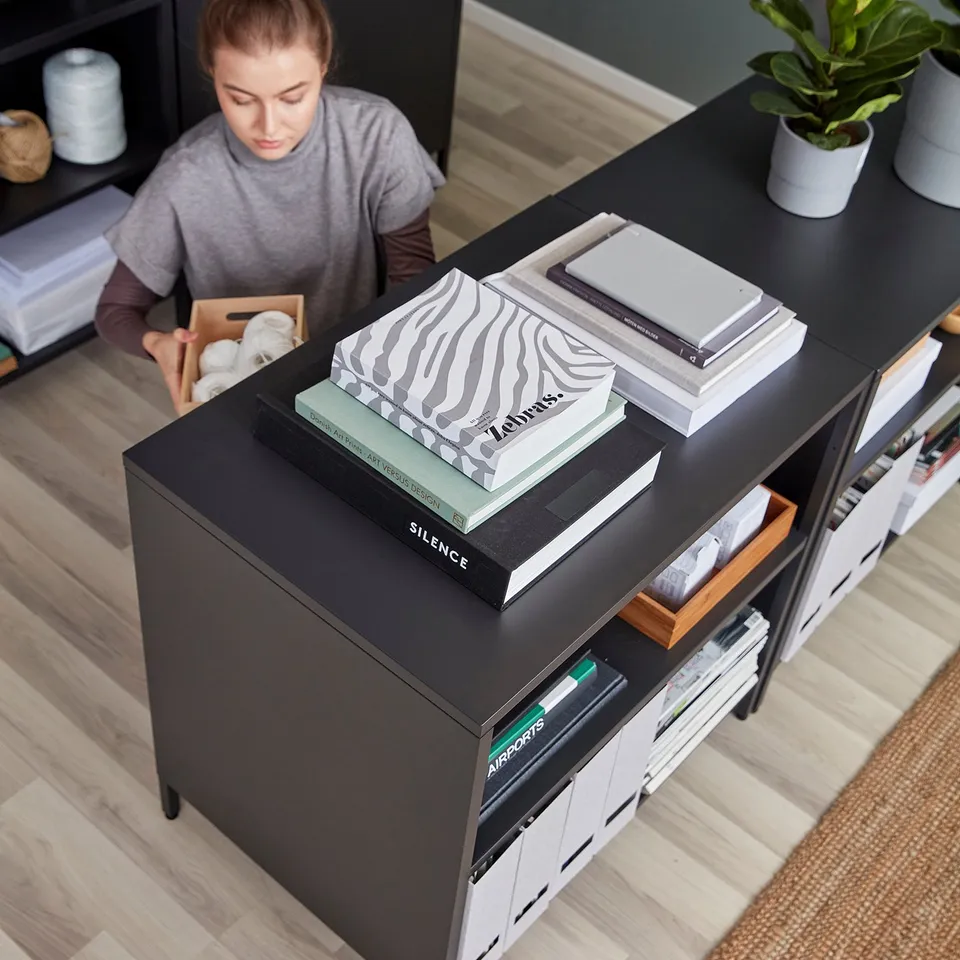 A person organises items on a trottan double-sided cabinet, divided as a room divider with adjustable shelves and lockable sliding doors.