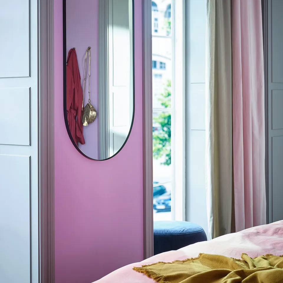 Bedroom with pink walls, LINDBYN black-framed mirror, red scarf, gold necklace, large window, pink curtains, and yellow blanket.