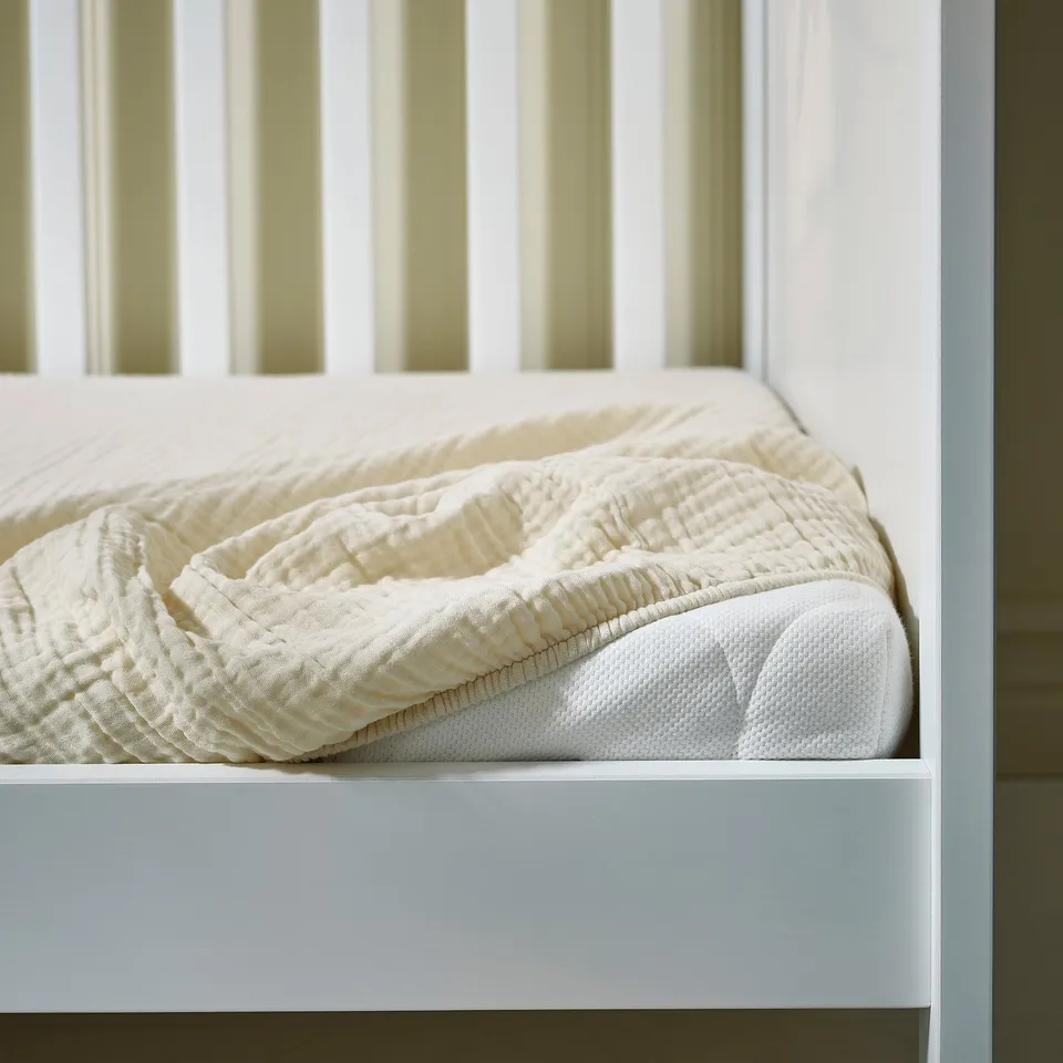A neatly made bed with a white blanket and pillow, perfect for a baby.
