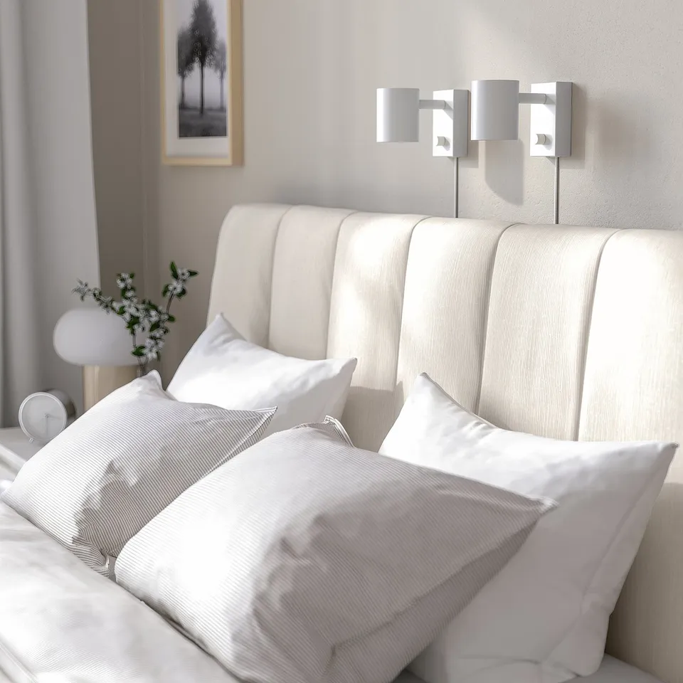 Modern white bed with padded headboard, two wall-mounted lamps, clean lined design.