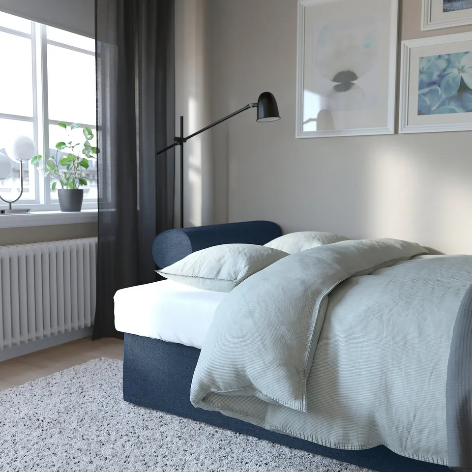 Bedroom with VRETSTORP sofa-bed, converted to bed, light grey bedding, pillows, and wall lamp on right.