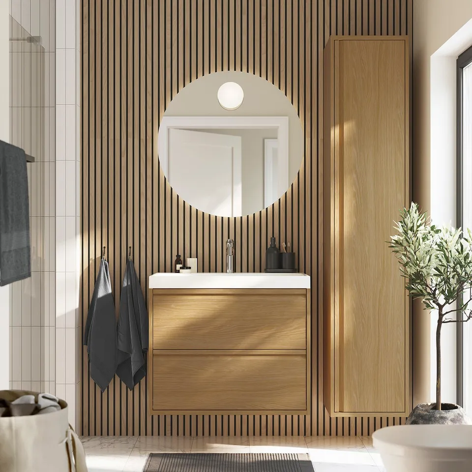 Modern bathroom with oak vanity, storage, round mirror, black accents, grey towels, plant.