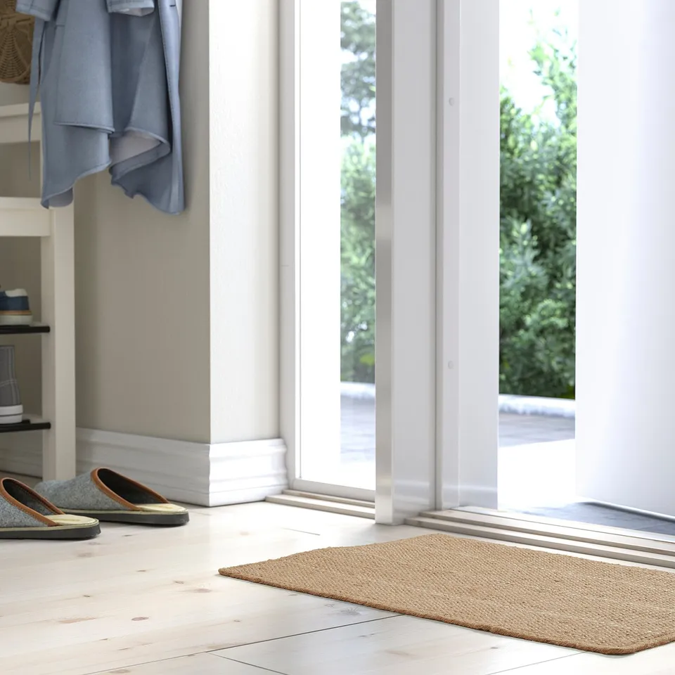 A bright entryway with a beige jute door mat, simple and natural, placed near an open white door, with two pairs of slippers beside it.