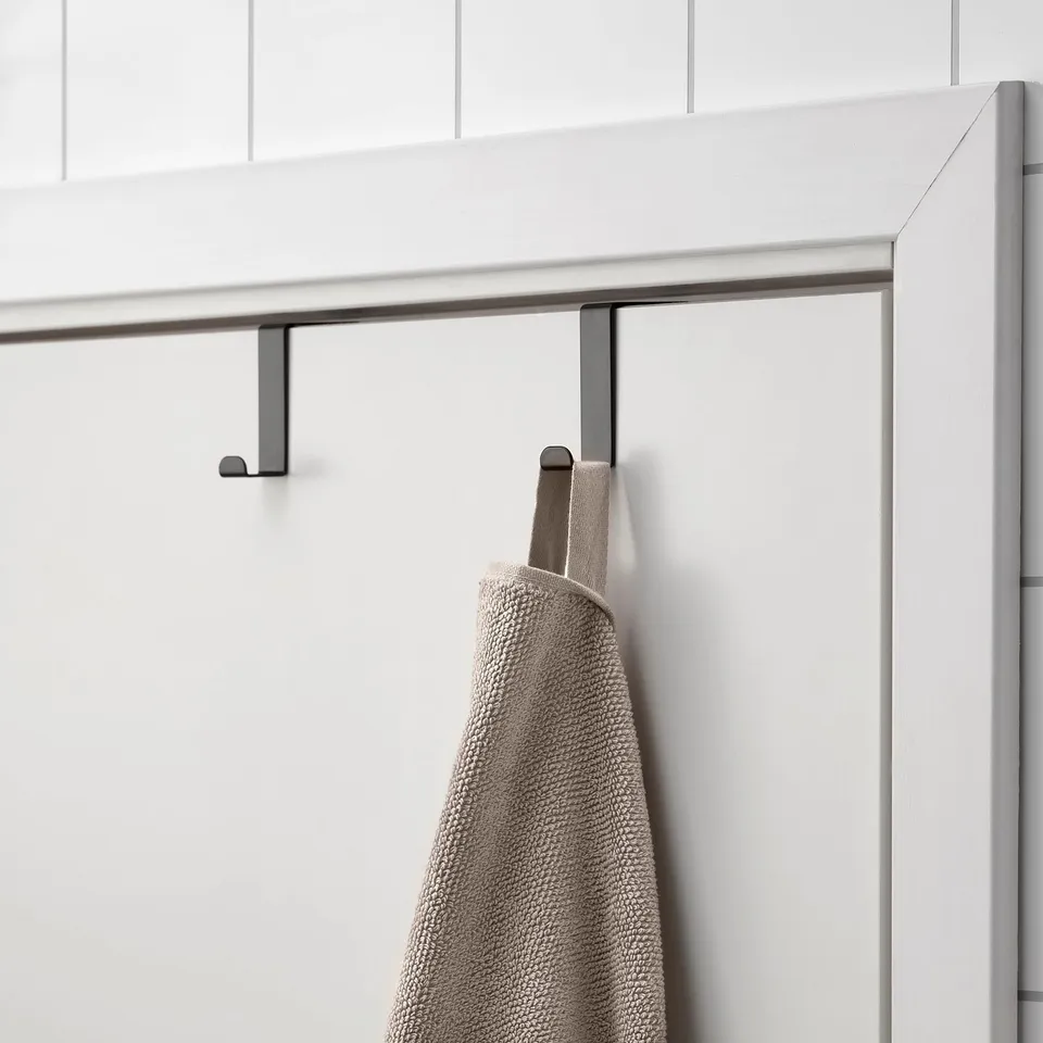 Black metal towel hook hangs over door, holding folded grey towel.