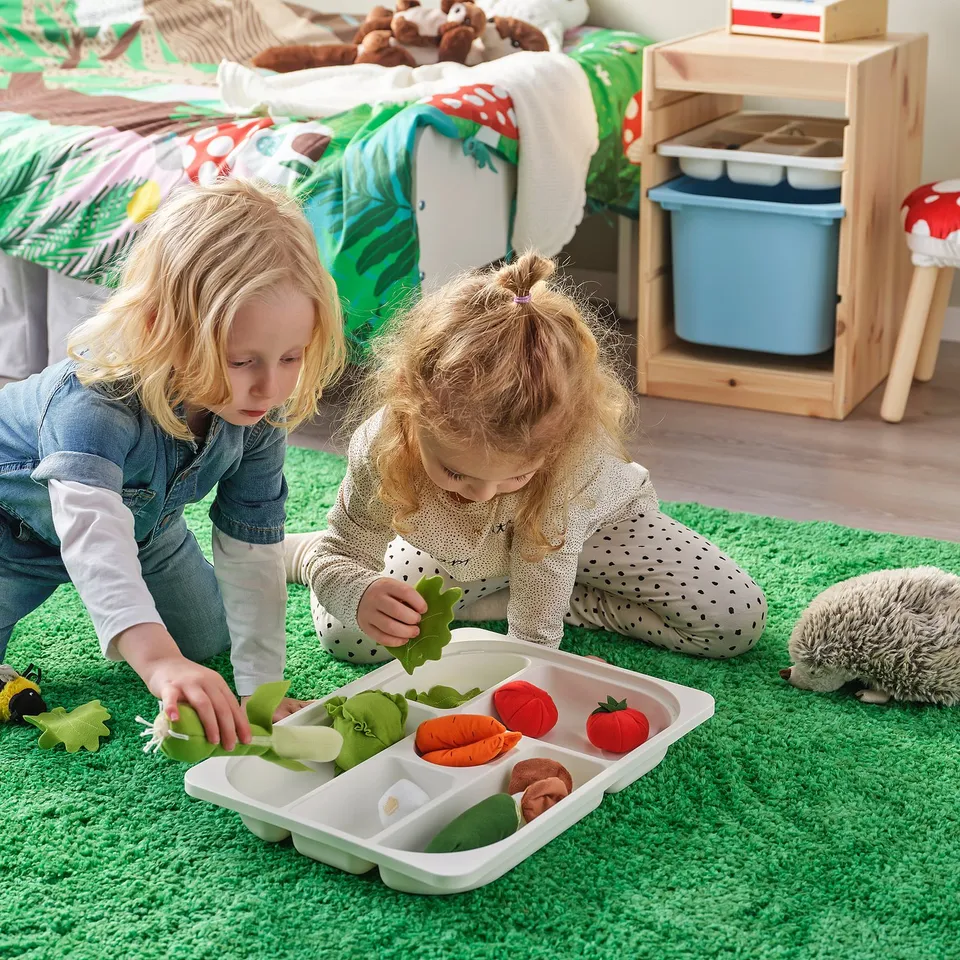 Children playing with toy vegetables in storage tray.