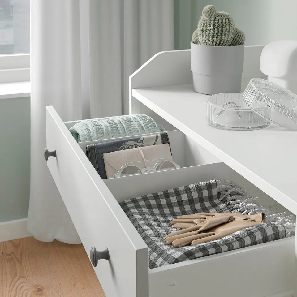 Open white HAUGA drawer displays neatly folded clothes and gloves on chequered fabric.