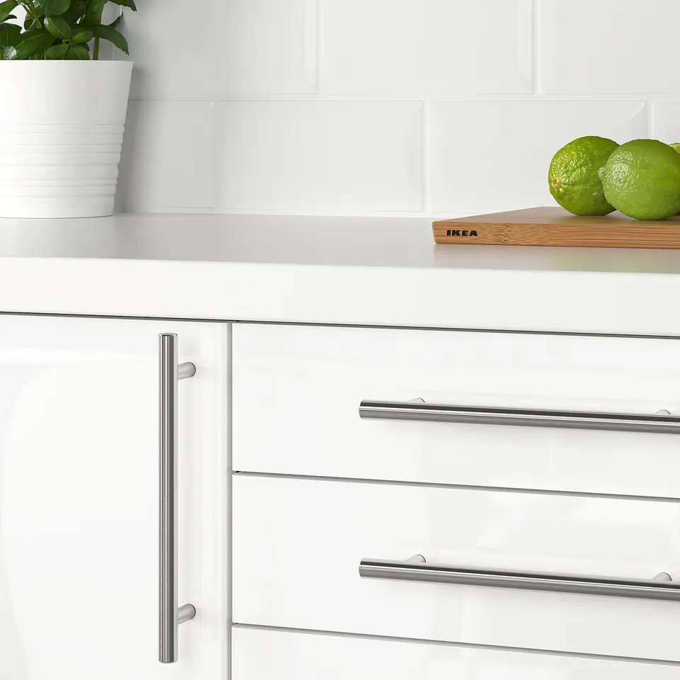 White kitchen cabinets with stainless steel KALLRÖR handles, limes on counter.