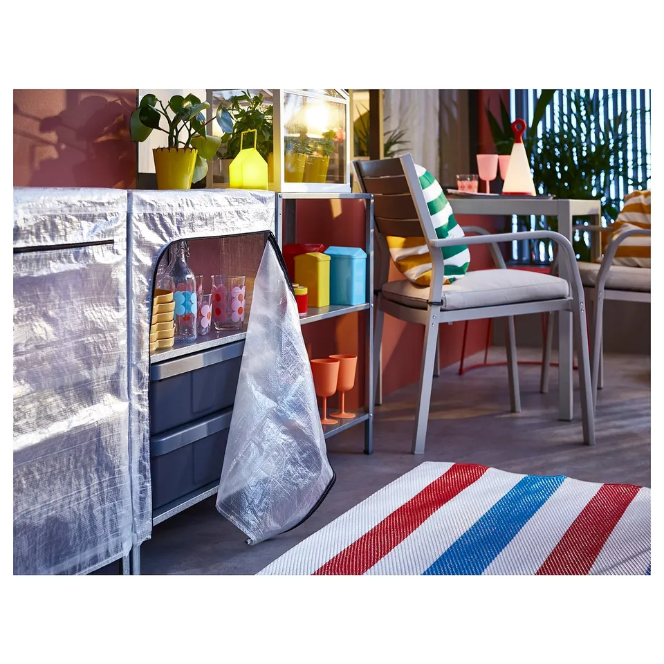 Bright patio with chairs, plants, and a shelving unit covered in a clear, protective, grey HYLLIS cover.
