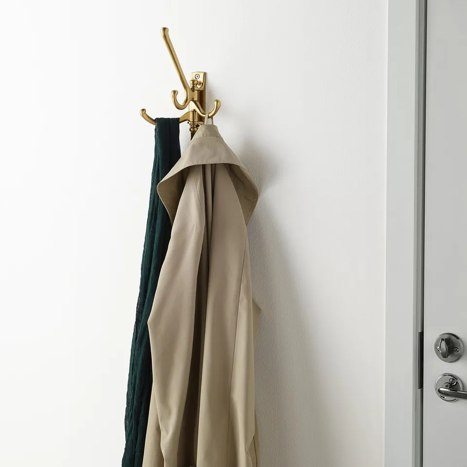 Gold coat rack with beige coat on wall near white door.