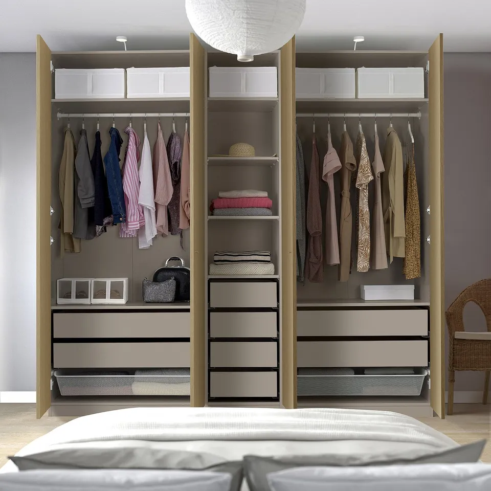Open wardrobe with clothes hangers and shelves, white bed in front.