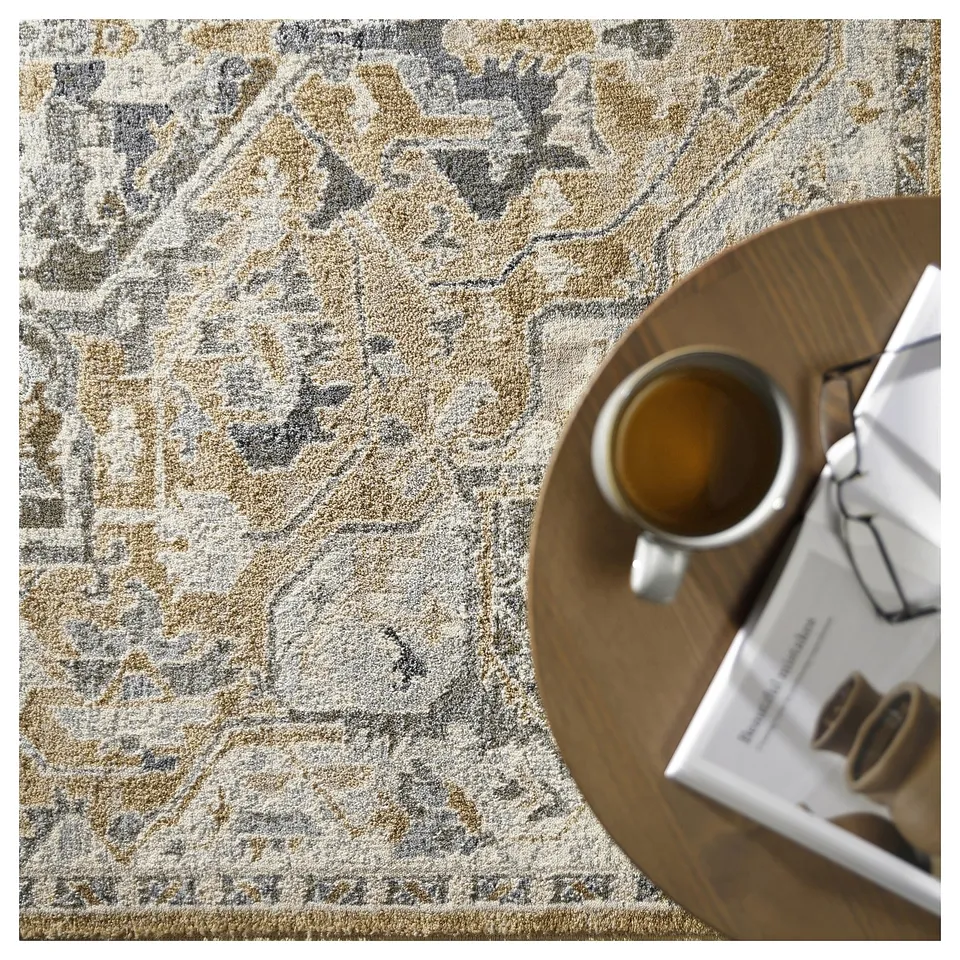 A beige and grey patterned rug, with a wooden round table holding a coffee cup and a magazine.