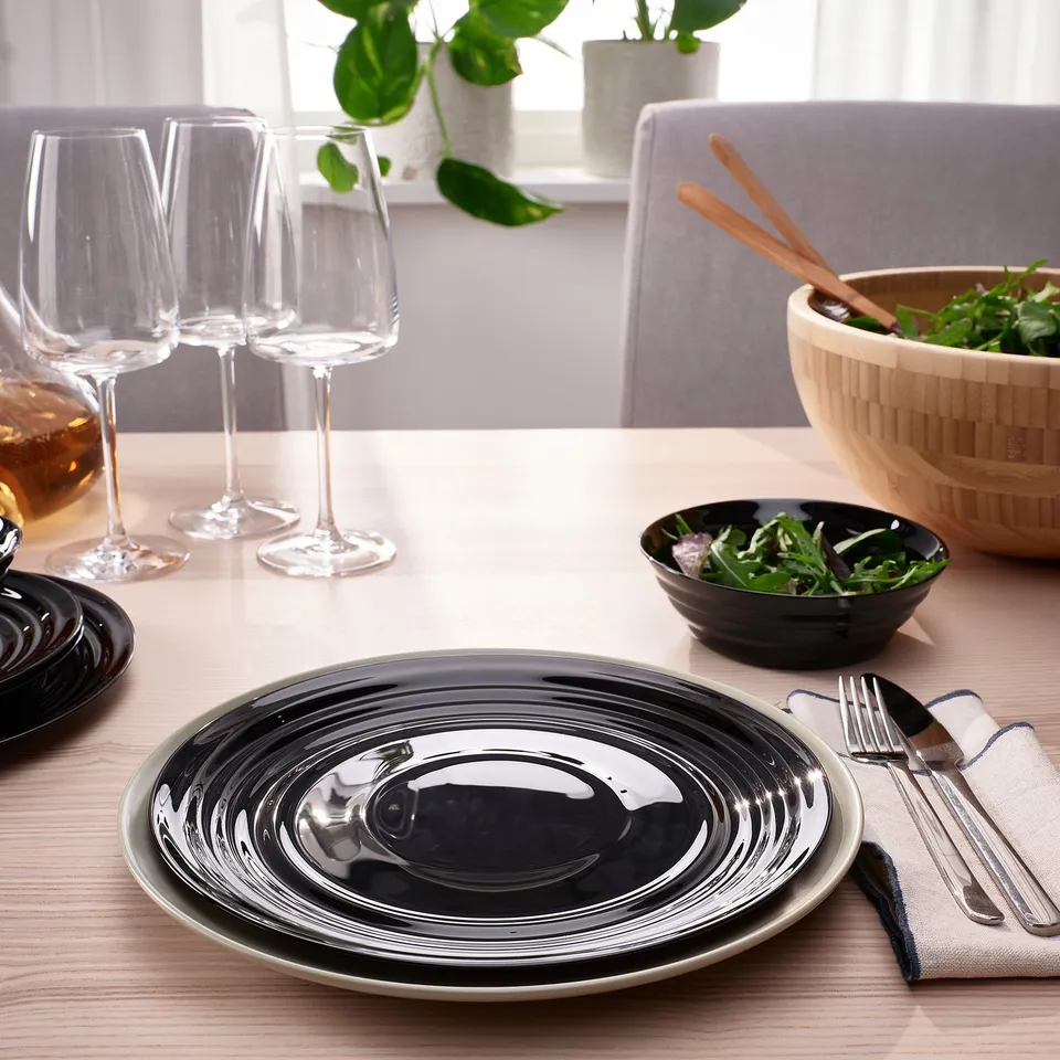 Table setting with glossy, patterned plates, glasses, cutlery, and bowls made of tempered glass. Ideal for elegant, easy-to-clean dining.