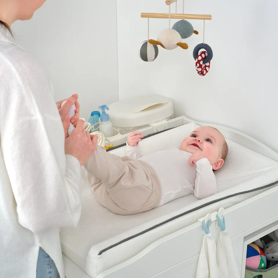 An adult tends to a baby on a changing table, which has practical storage and safety.