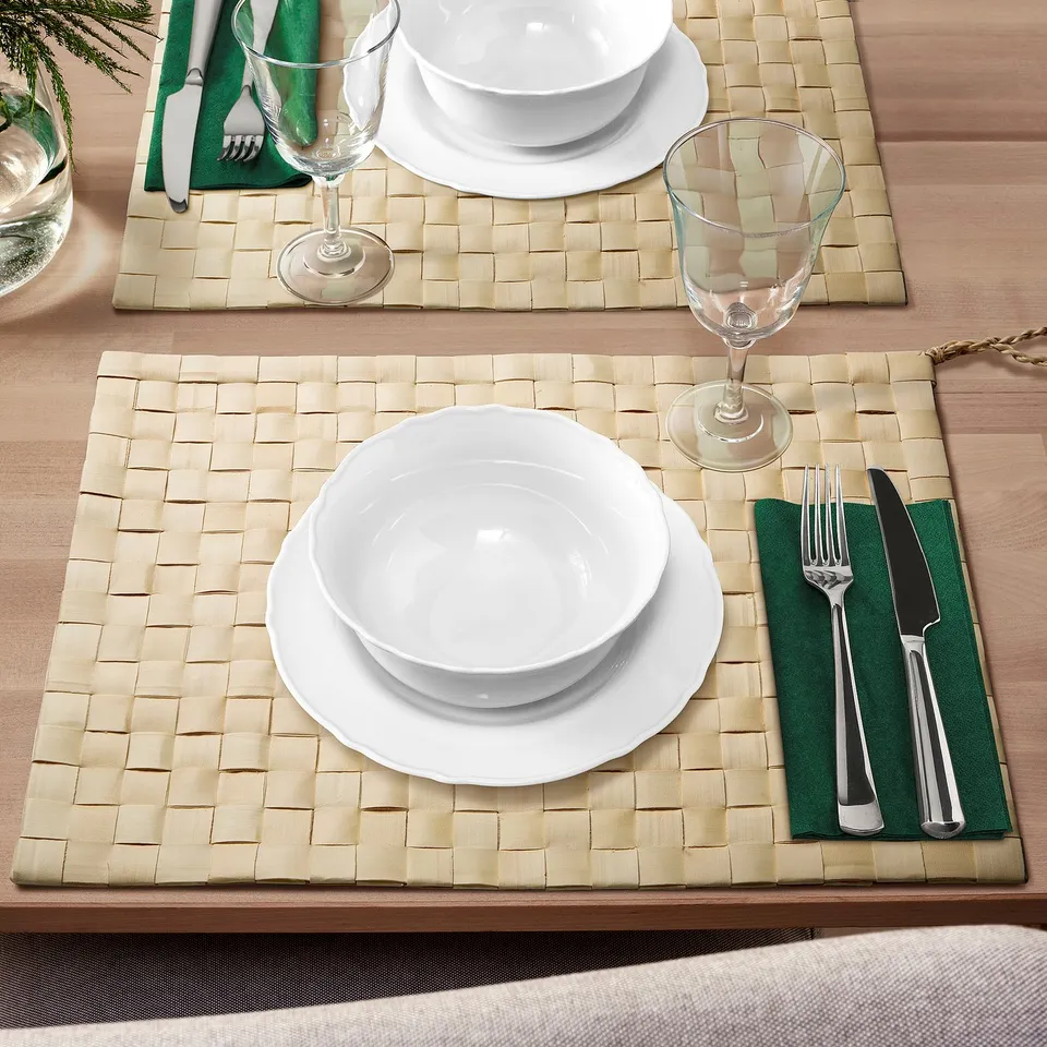 Handwoven MÄVINN placemats, natural beige with dishes, cutlery, and wine glasses.