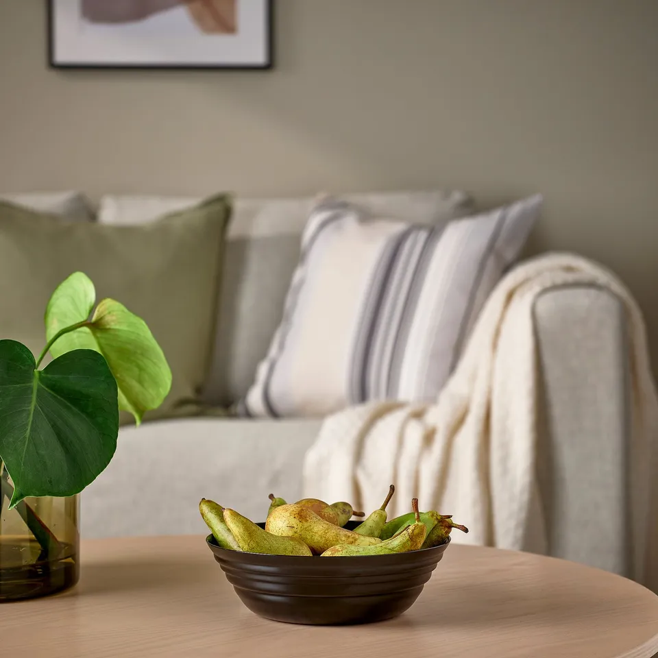 Cosy living room with NÄTBARB bowl of fruit on wooden table, near plant, and modern couch.