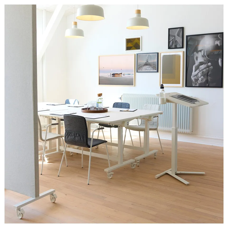 Modern office meets contemporary art. White MITTZON tables and chairs surround wooden floor, under hanging lamps. Art prints adorn walls.