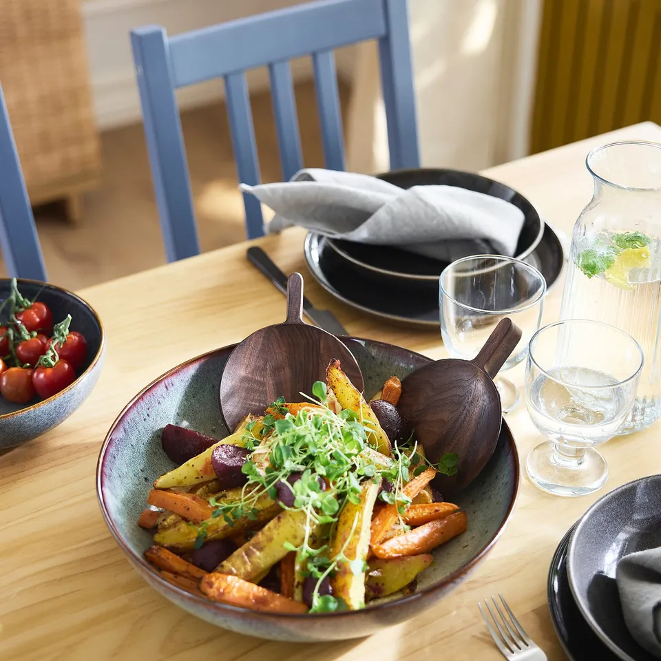A rustic wooden table with blue chairs, set with a bowl of veggies & glassware.