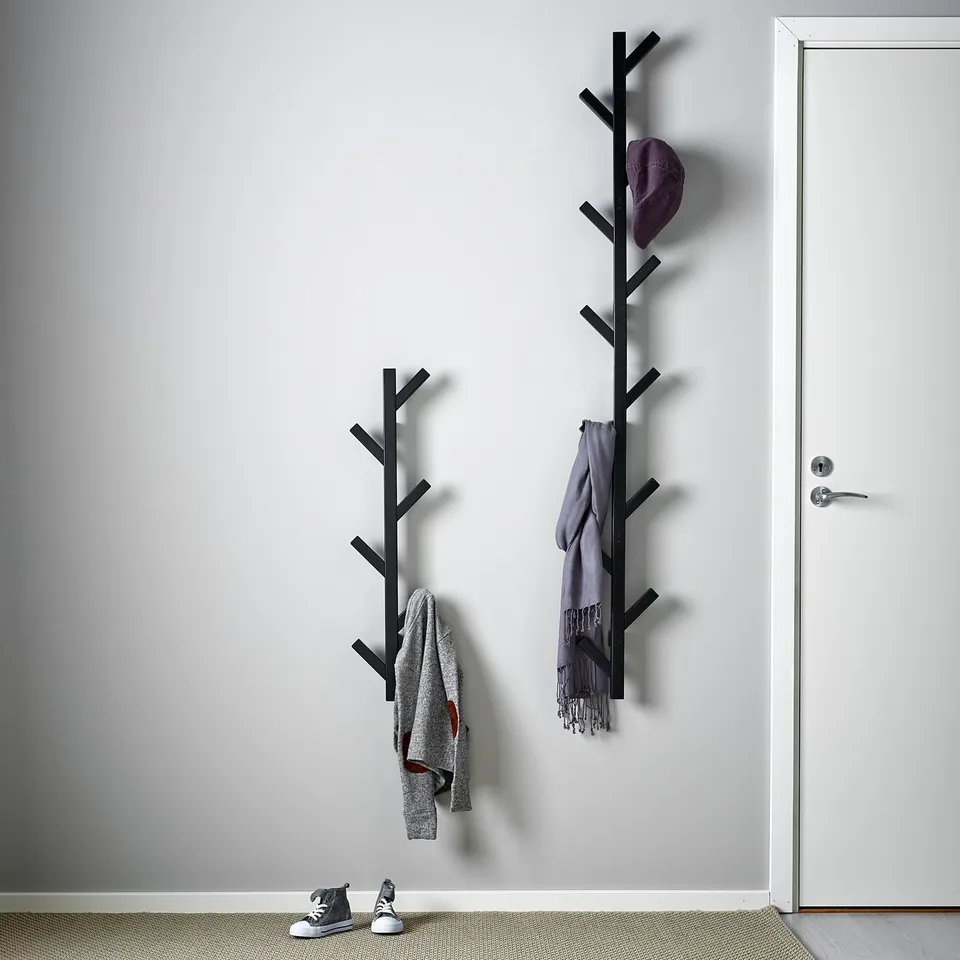 Wall-mounted coat rack with hooks, holding jackets and a hat, next to a door.