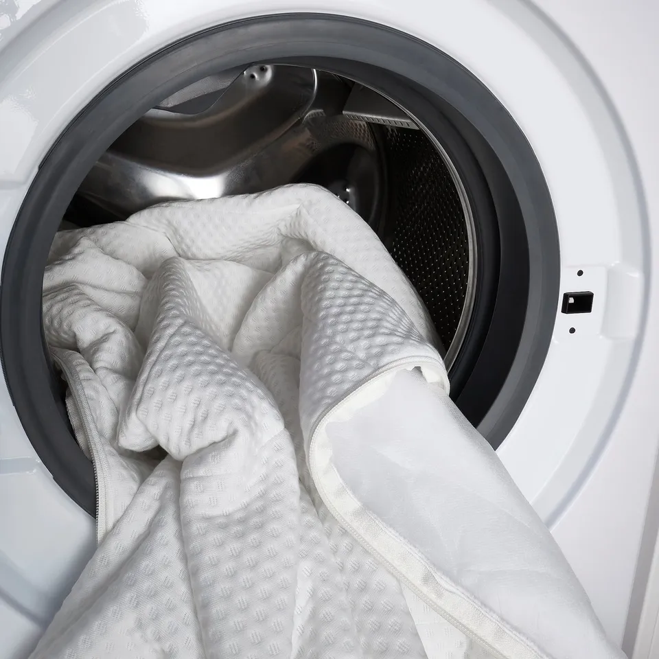 Washing machine door open, holding white blanket inside, ready to clean.