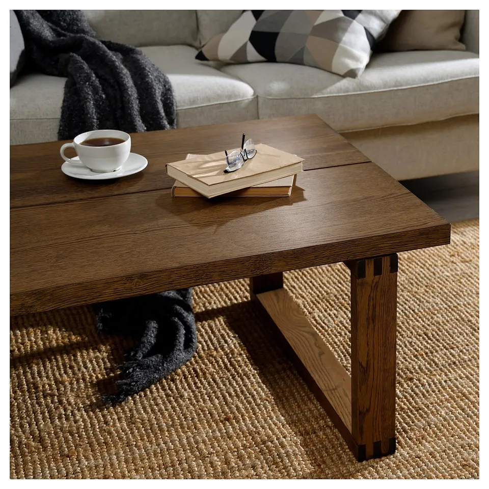 Wooden coffee table with cup, book, and glasses atop; light, natural wood grain; smooth surface.