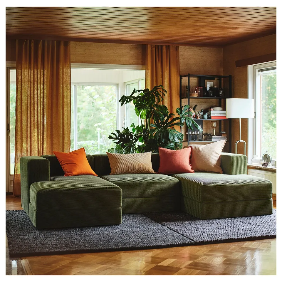 Cosy living room with JÄTTEBO green modular sofa, vibrant pillows, large plant, wooden decor, sunny window.