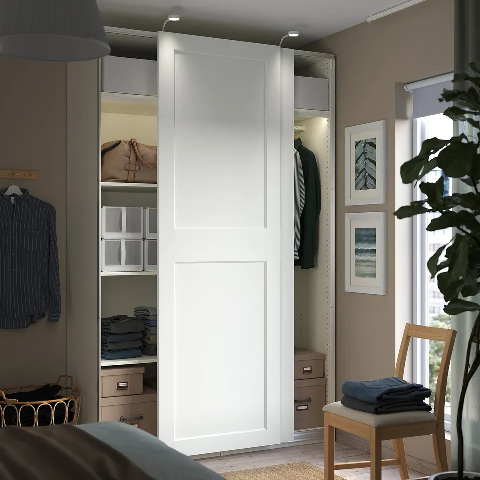 Modern bedroom featuring white PAX wardrobe with sliding doors and organised storage, including shelves and drawers.