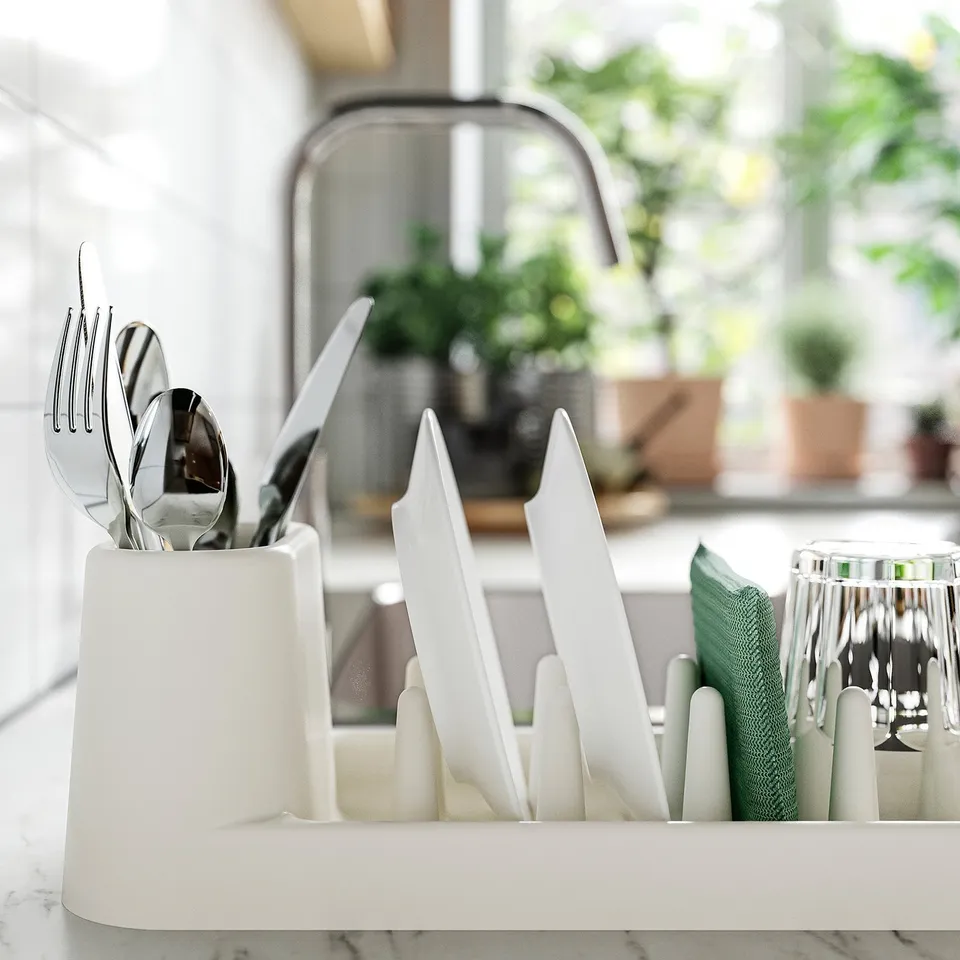 White dish drainer holds plates, glasses, and cutlery; collects run-off water at the bottom.
