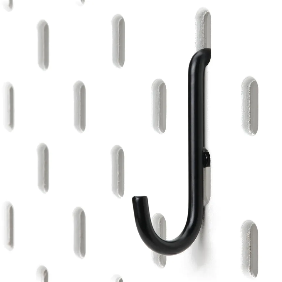 Black metal hook firmly attached to a white pegboard with evenly spaced holes, demonstrating robust and minimalist design.