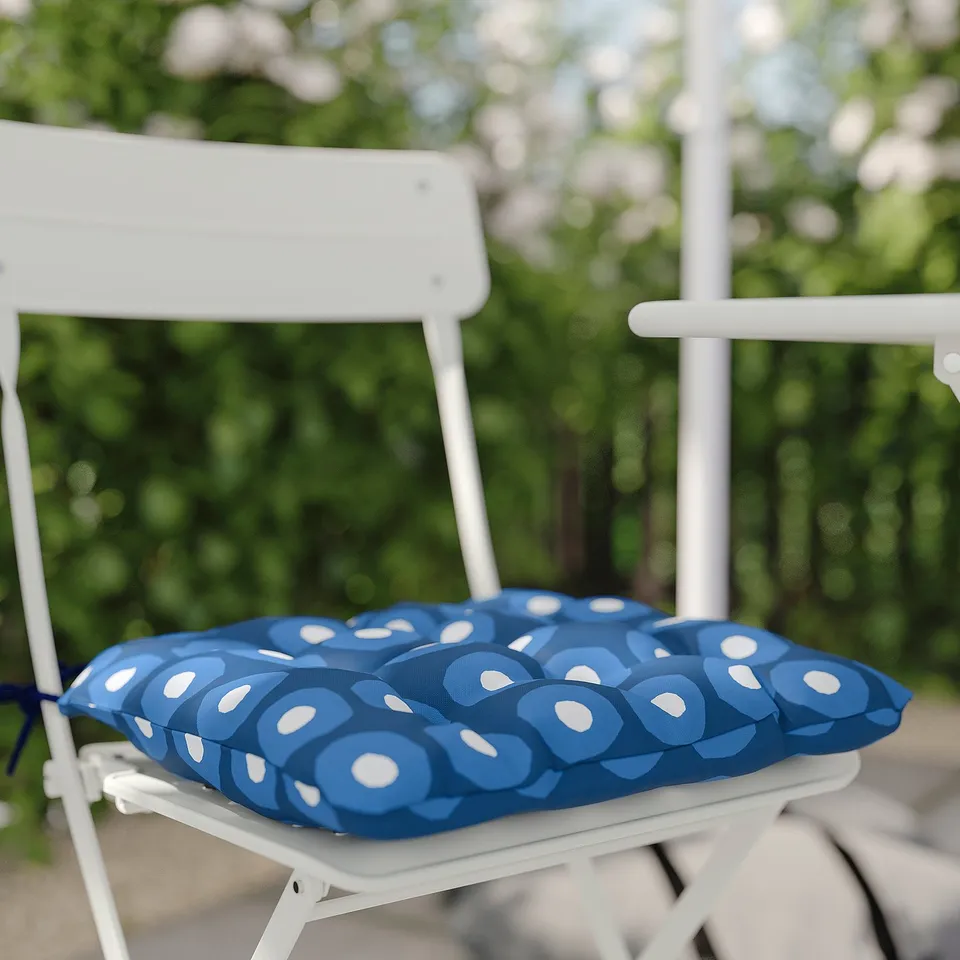 A white SUNDSÖ folding chair with a blue patterned cushion outdoors.