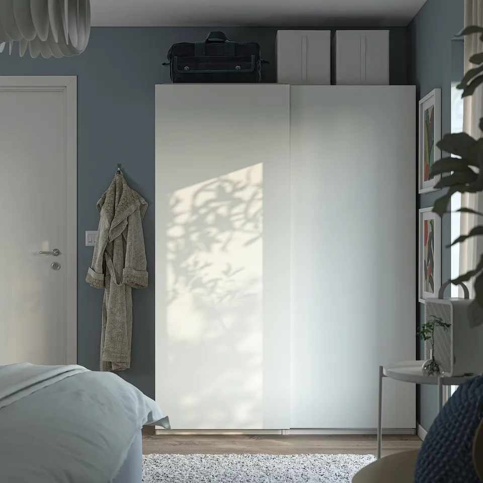 PAX wardrobe: white, tall, sleek, with sliding doors; fits corner, nearby door, bed, plant stand.
