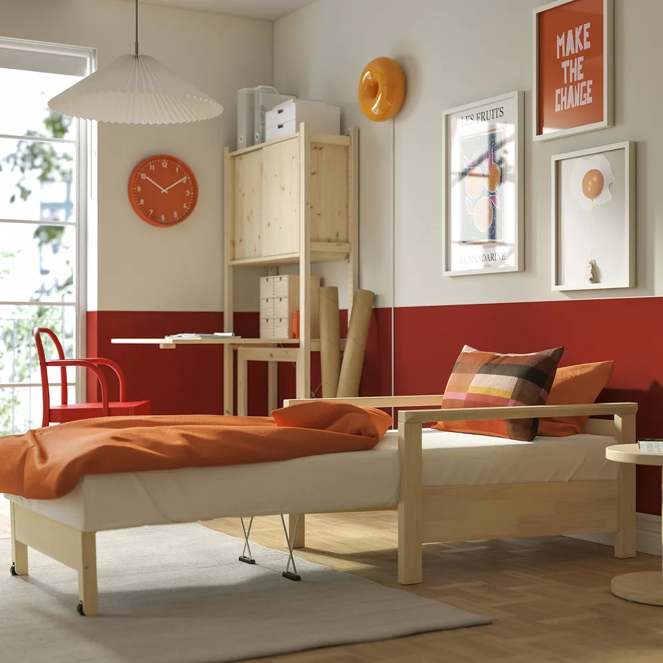 Modern room with TORNSBORG bed-armchair, red blanket, colourful pillows, and orange accents. Wall clock and artwork decorate the space.