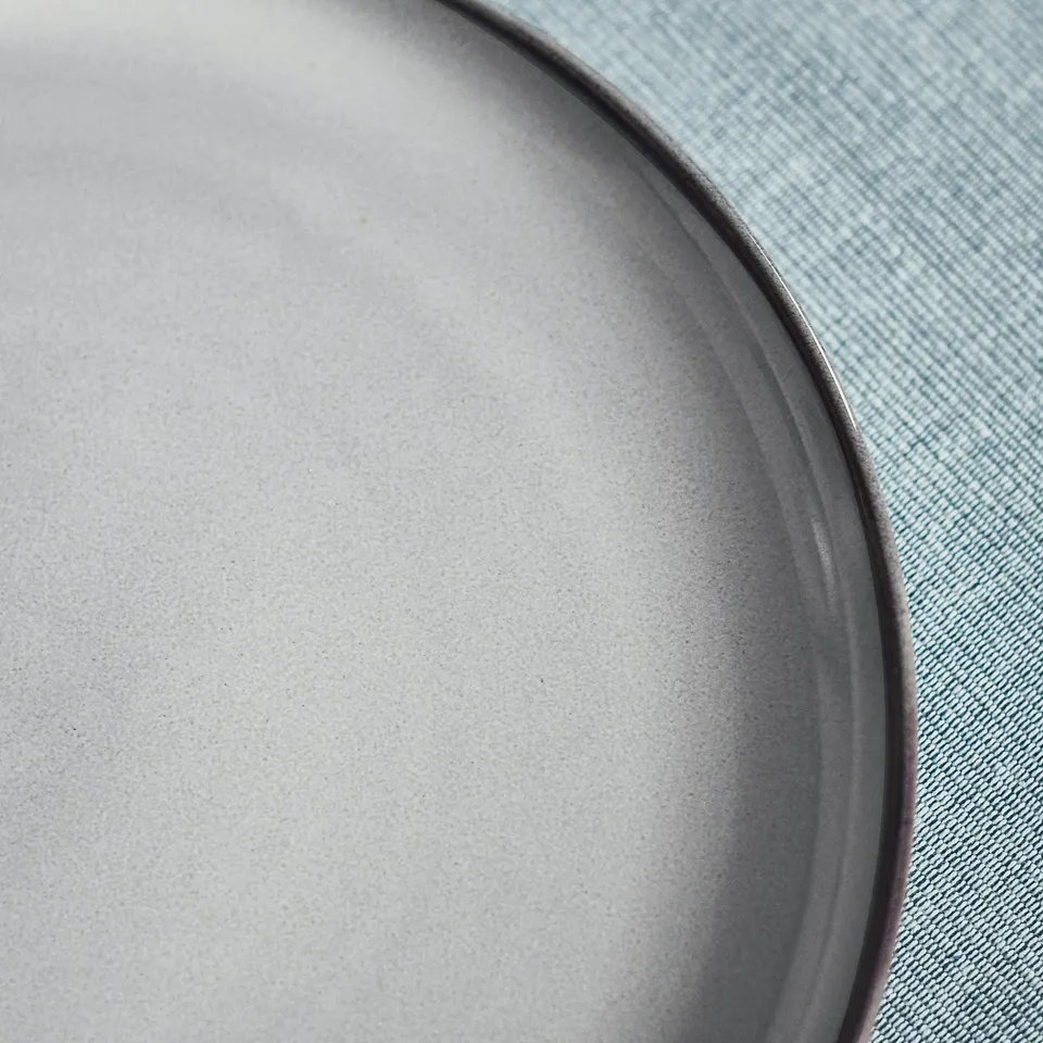 Close-up of a stylish, handcrafted stoneware plate with a reactive glaze, resting on a light blue denim surface.