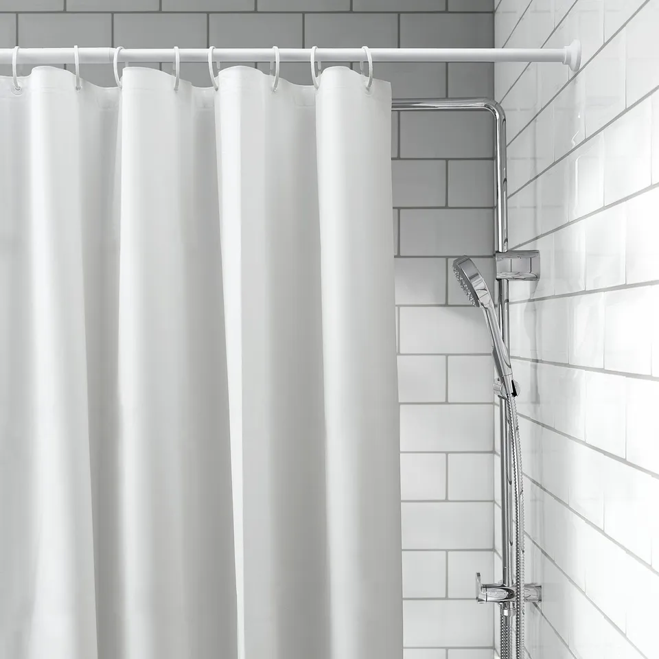 White shower curtain with hooks hangs on a rod, fine water drops. Attached is a handheld shower head on a holder. Set in light grey tiled bathroom.