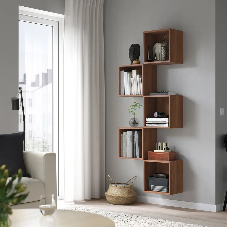Modern living room with wall-mounted EKET shelves, books & decor. Asymmetrical design near bright window & white couch.