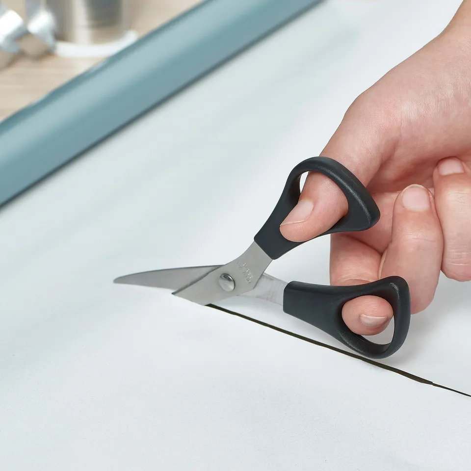 Hand cuts white paper with MÅNÖGA scissors, designed for both right and left-handed users.