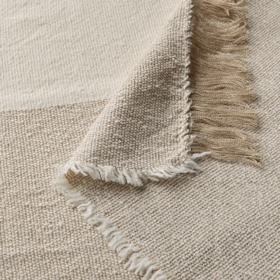 Soft, fringed throw blanket in cream with fine weave pattern. Lightweight and cosy, made from recycled materials.
