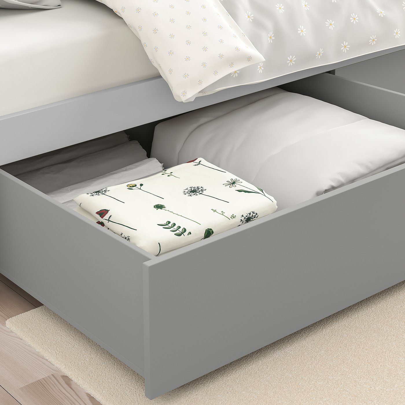 Bed drawer under a white bed, storing floral-patterned folded sheets. Part of SMYGA series for organising under-bed space efficiently.