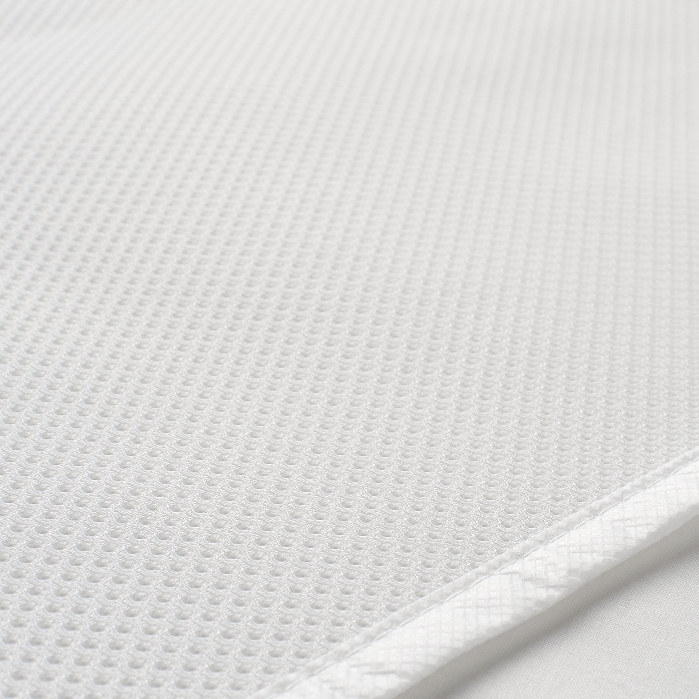 Close-up of a textured white mattress protector, showing its ventilated mesh surface with evenly distributed small holes.